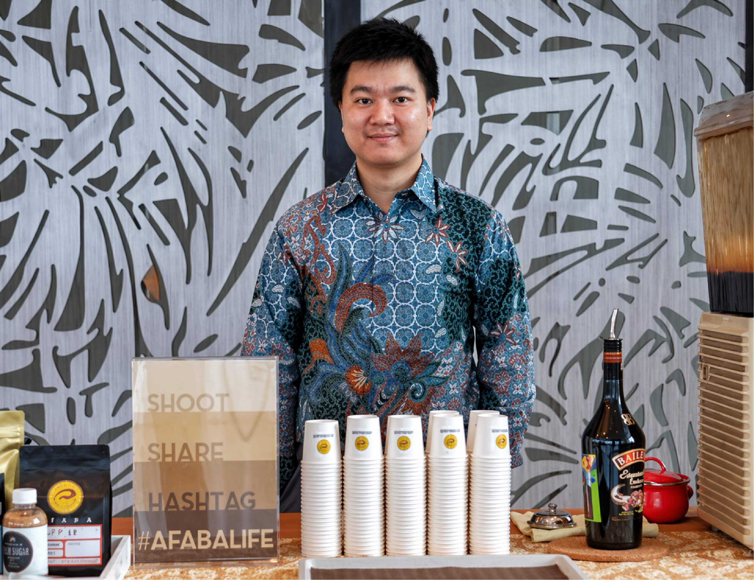 Coffee professional standing behind cupping setup with stacked cups and coffee products display