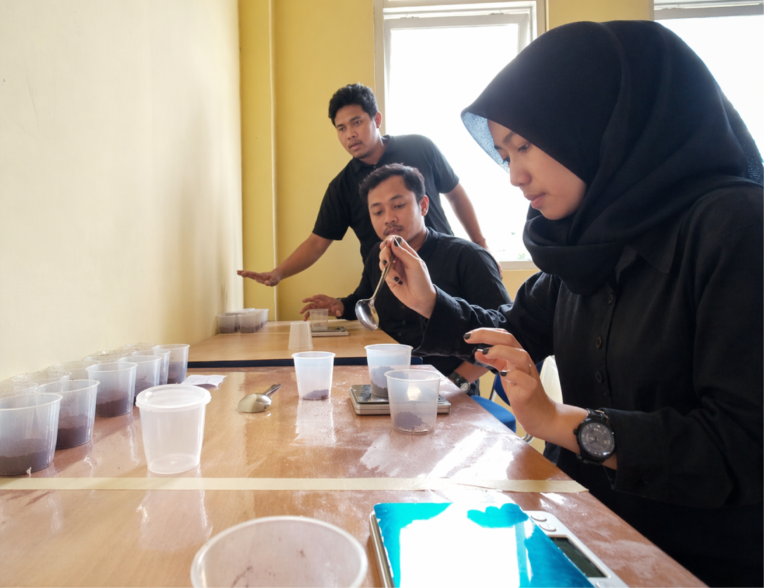 Coffee cupping session in Indonesia with a woman in black hijab and two men evaluating coffee grounds using professional tasting methods